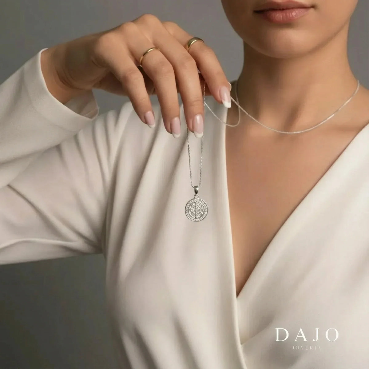 Mujer con blusa blanca sosteniendo una cadena delgada de plata .925 con la medalla de San Benito de DAJO