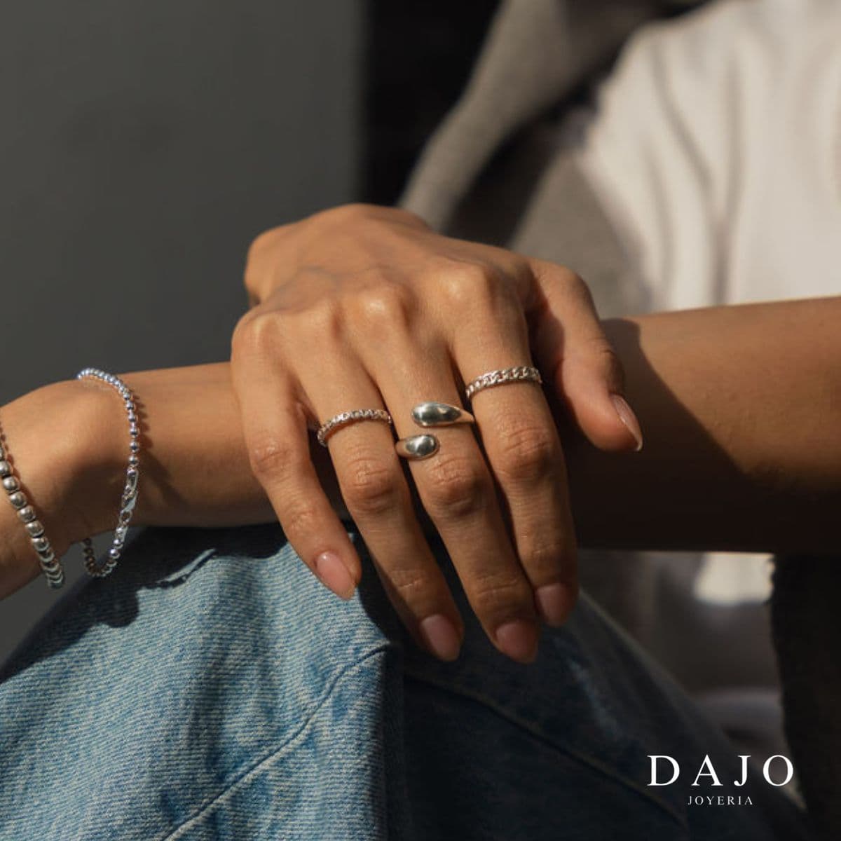 Modelo mujer senada usando combinación set de joyería anillos plata .925 estilo urbano street jeans mezclilla