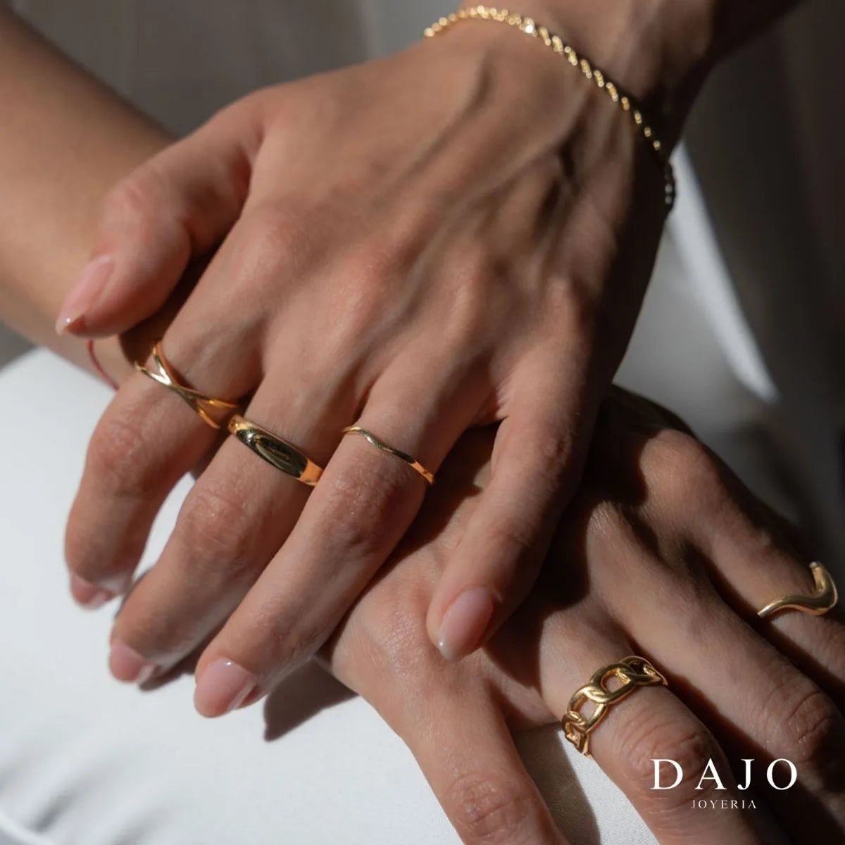 Modelo mujer usando combinación set layering de joyería anillos y pulsera Oro Vermeil plata .925 con baño de oro de 14K quilates estilo elegante traje blanco. Manos en rodilla