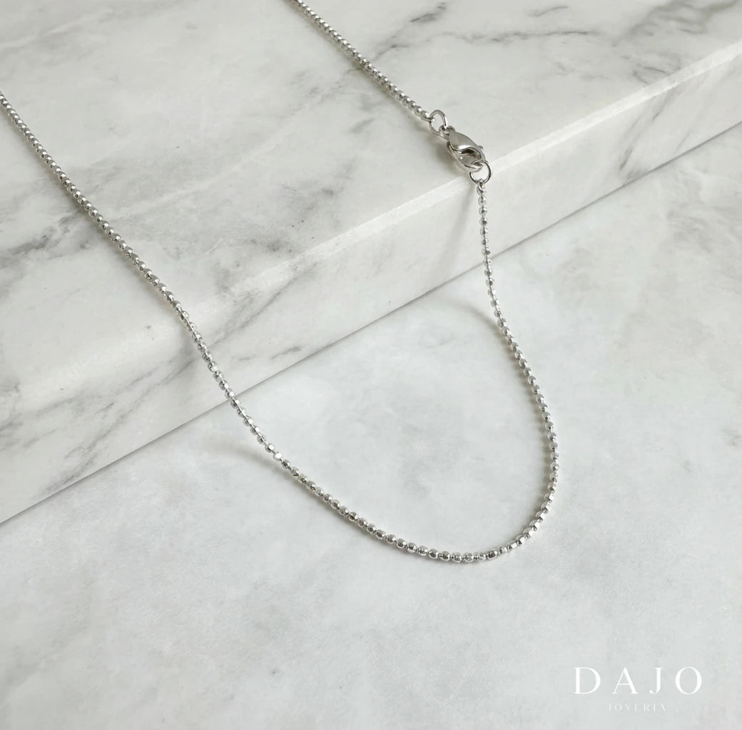 Esta cadena de plata .925 está formada por pequeñas esferas de 1 mm con caras planas, lo que le da un brillo extra al moverse (como un mini dodecaedro).
Es delgada, minimalista y con un toque original gracias a su textura poco común.
Ideal si buscas una cadena sutil, diferente y que atrape la luz de forma elegante