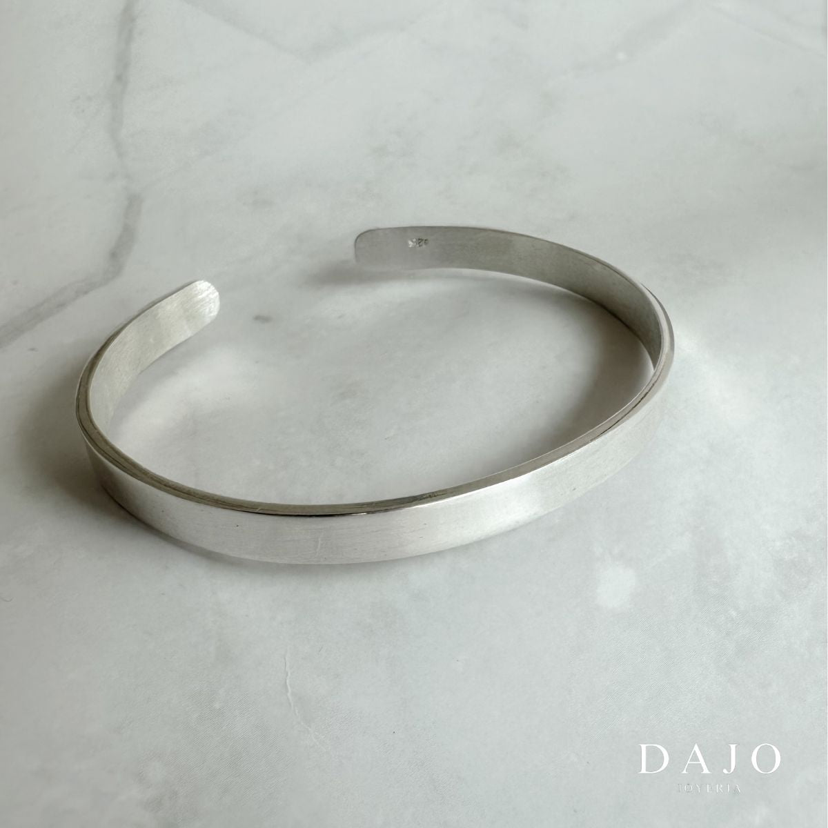Este brazalete en plata .925, con su diseño en forma de "U" y un ancho de 6 mm, encarna la esencia del minimalismo estético: líneas limpias y funcionalidad sin adornos superfluos. Su elegancia discreta resuena con la estética "old money", que valora la sofisticación atemporal y la calidad sobre la ostentación. La pieza proyecta una imagen de refinamiento y buen gusto, ideal para quienes aprecian la moda clásica y la artesanía de alta calidad
