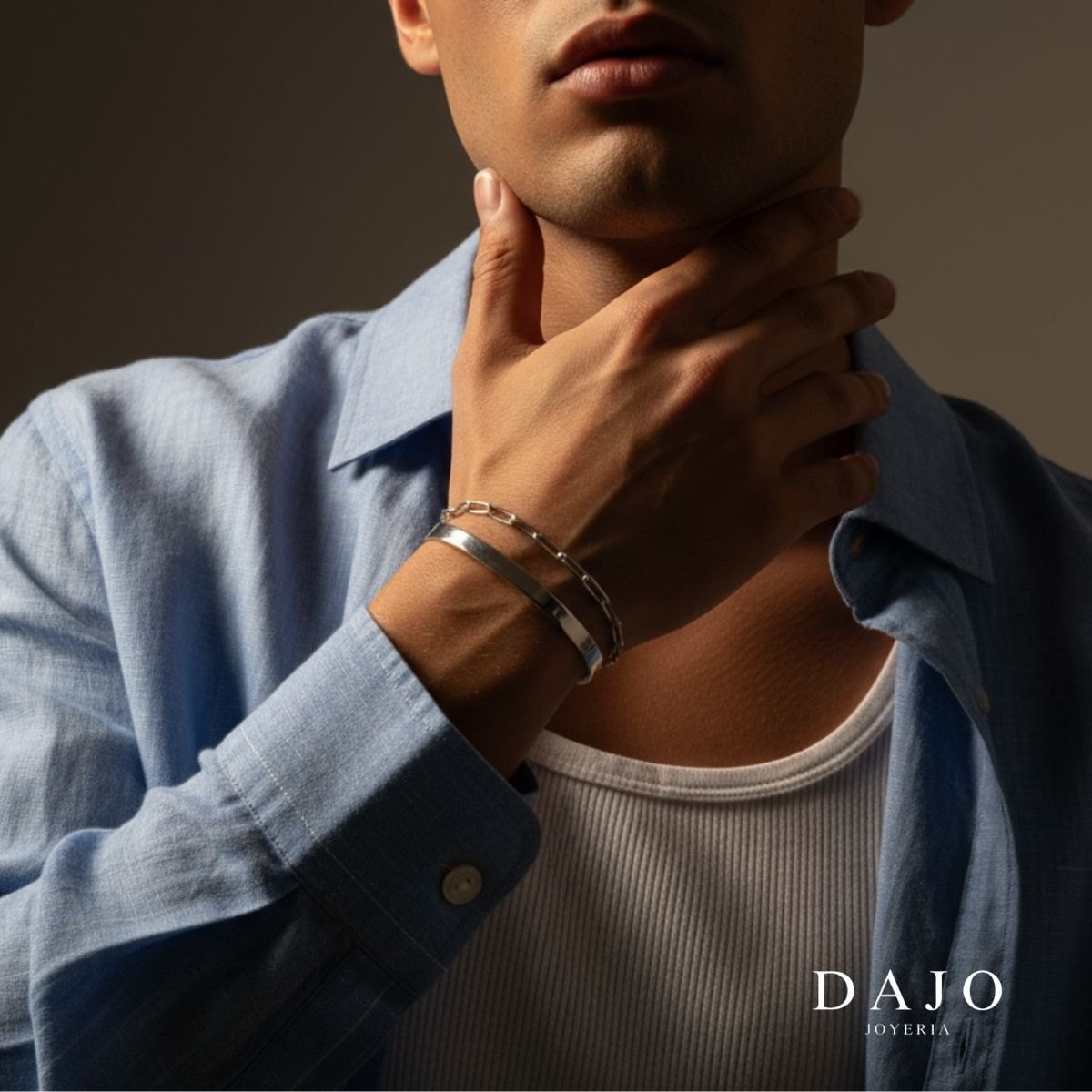 Brazalete Liso de plata .925 puesto en la muñeca de un hombre con camisa azul, junto a una pulsera de eslabones, de DAJO Joyería