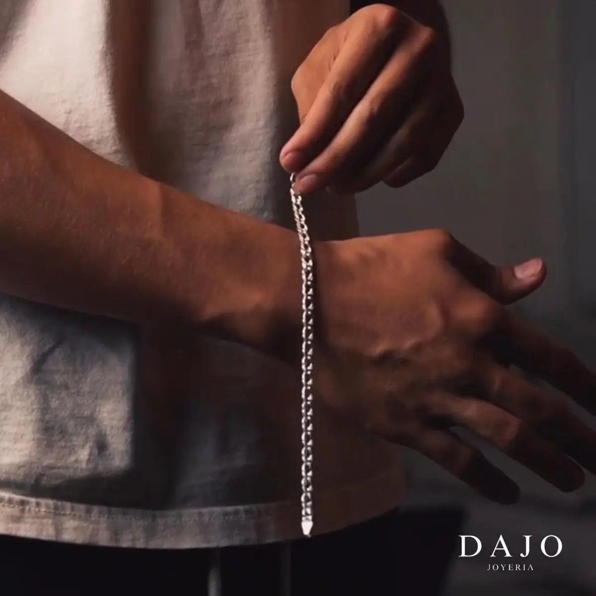 Modelo hombre con pulsera de plata .925 artesanal mexicana en muñeca. Playera blanca. Abrochando pulsera. Ideal para regalo o uso personal.