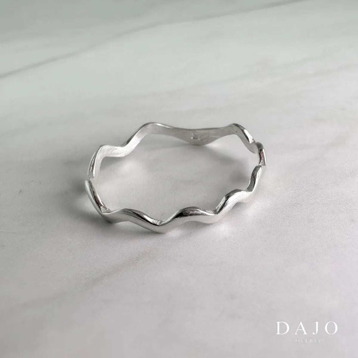 Anillo Waves de plata .925, destacando la elegancia y la fluidez de su diseño inspirado en las olas del mar sobre mármol gris