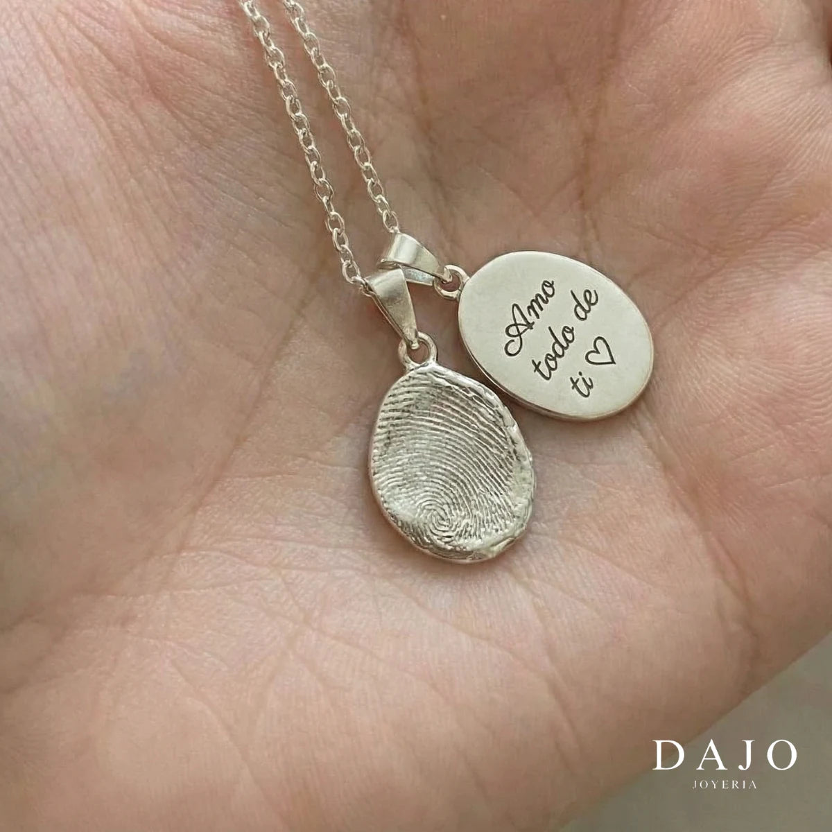 Dije Huella de plata .925 en forma de gota junto a un dije con la frase «Amo todo de ti» grabada, en la mano