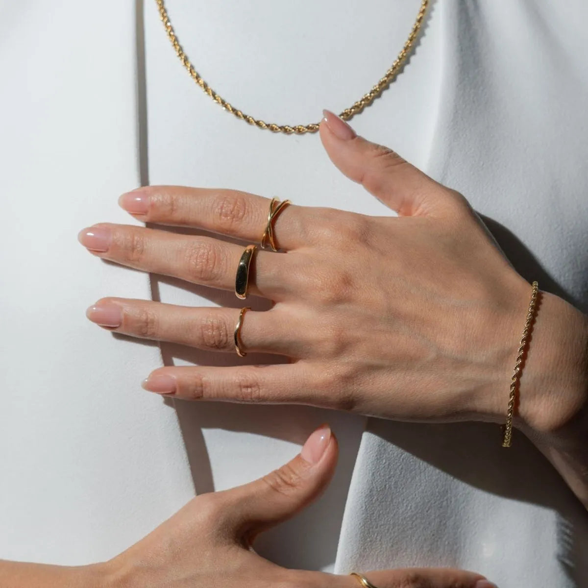 Modelo mujer usando combinación set layering de joyería anillos y collar Oro Vermeil plata .925 con baño de oro de 14K quilates estilo elegante traje blanco. Manos en pecho