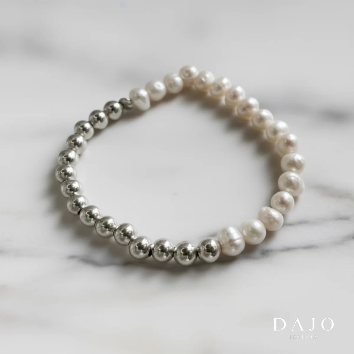 Esta pulsera combina esferas de plata y perlas barrocas, unidas mediante una banda elástica que garantiza comodidad y adaptabilidad.

Las perlas barrocas, conocidas por sus formas únicas e irregulares, aportan un carácter distintivo a la joya, mientras que las esferas de plata añaden un toque de brillo y sofisticación.