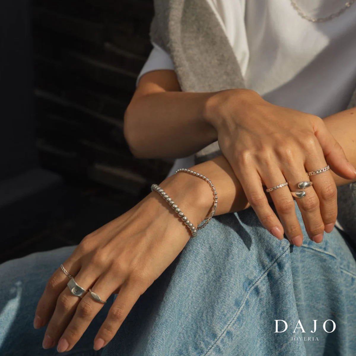 Modelo mujer usando combinación set de joyería anillos plata .925 estilo street jeans mezclilla sentada. Anillo infinito irregular botanica