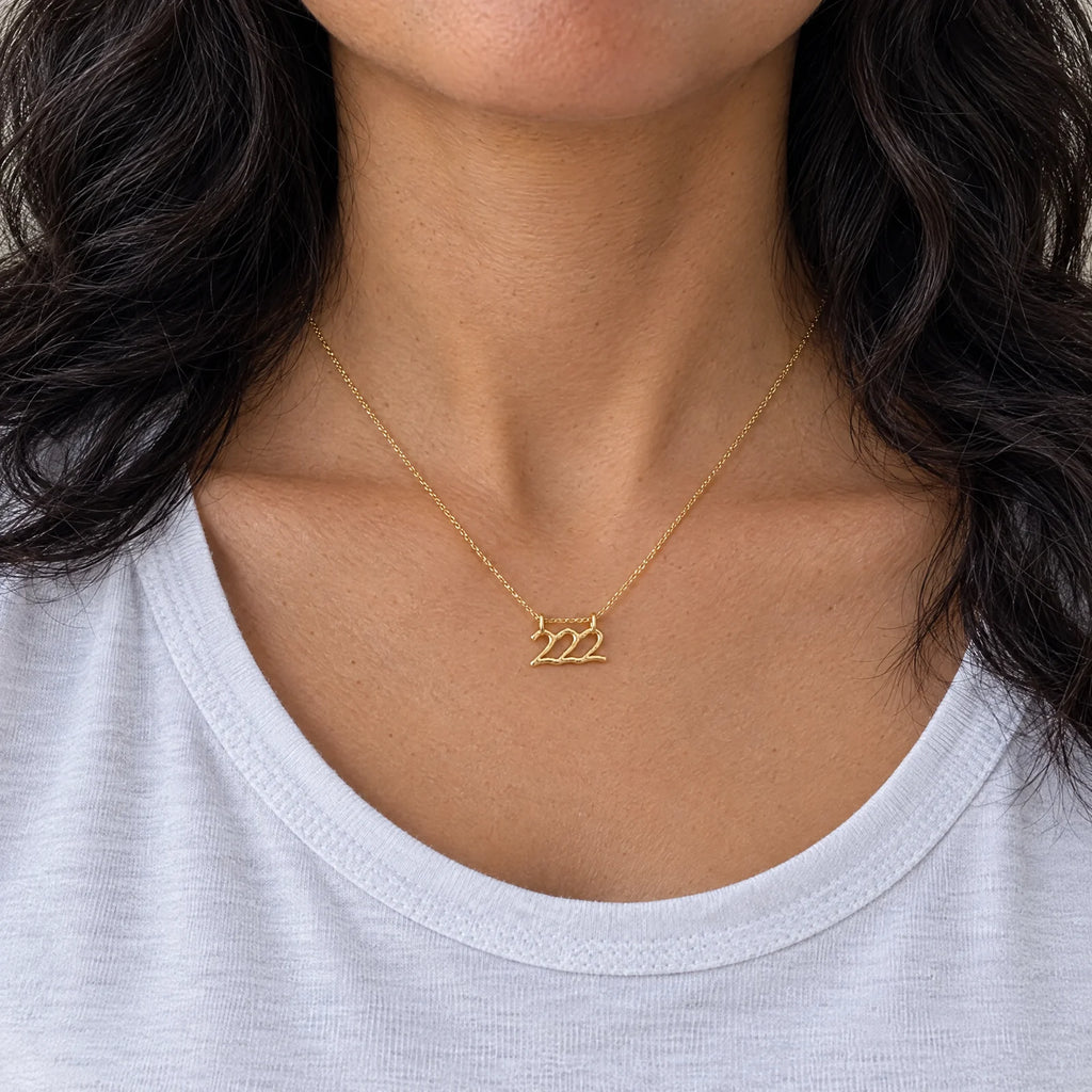 Dije Número Ángel 222 de oro sólido de DAJO puesto con playera blanca, a su tamaño real de 17 x 9 mm