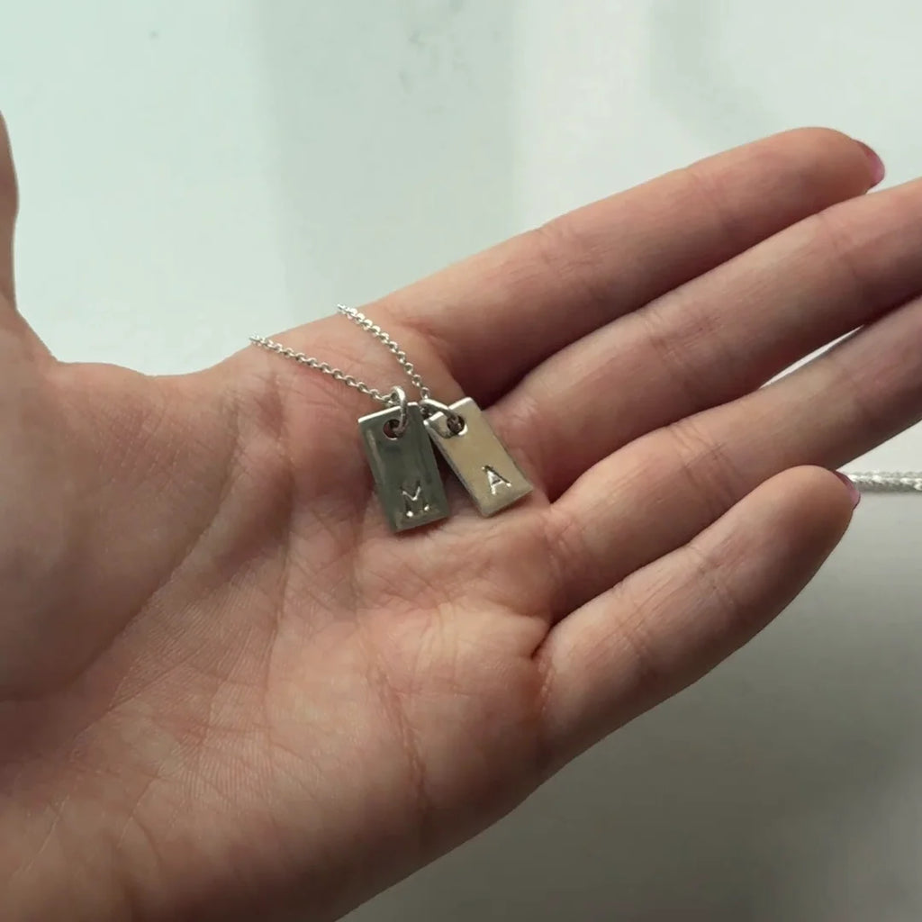 Dos dijes marco de plata .925 en la palma de la mano, una inicial en cada uno