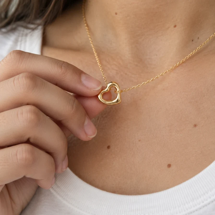 Dije Corazón Irregular de oro sólido de DAJO sostenido entre los dedos, 11 mm de ancho