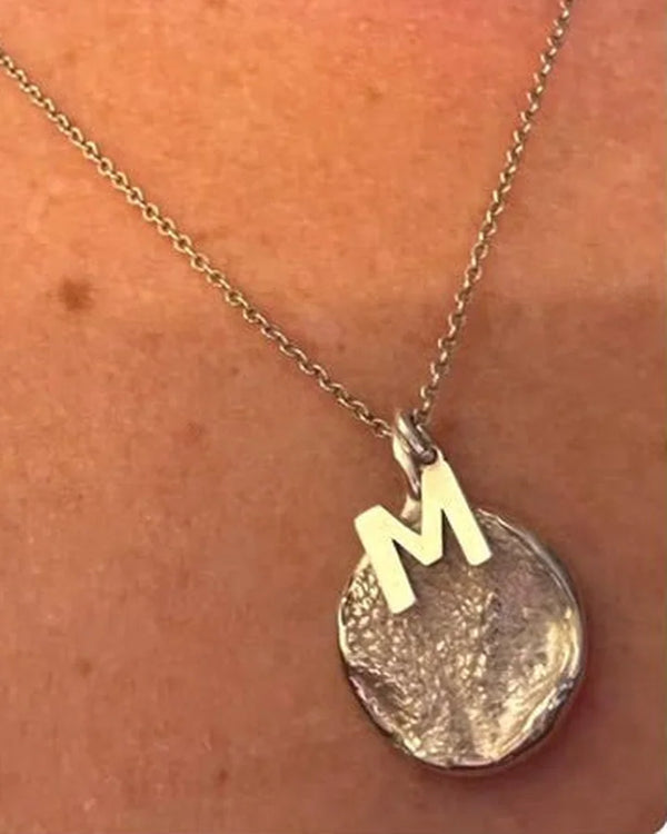 Dije de plata con la huella de una perrita y la inicial M, puesto al cuello