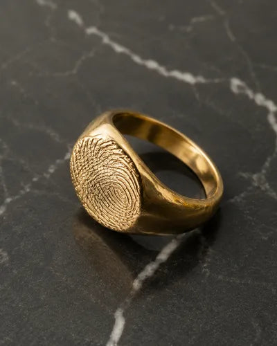 Anillo sello redondo de oro con huella, de tres cuartos, sobre mármol negro